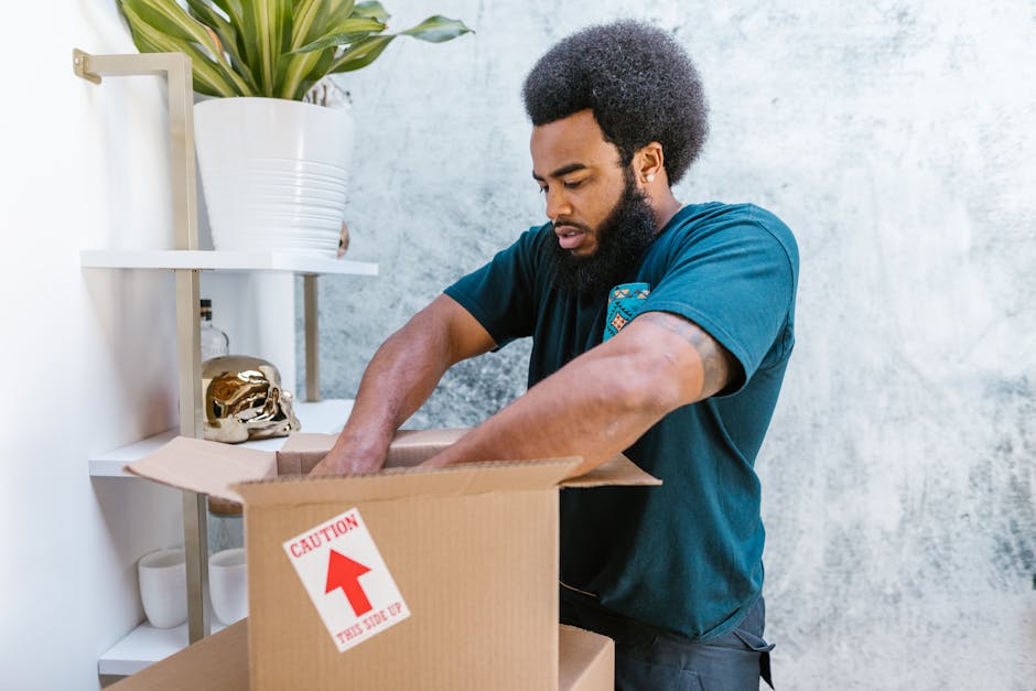 A professional mover from tomsremovals.co.uk is engaged in the home relocation process, carefully carrying a green upholstered sofa through a door opening inside a residential property. The mover is w